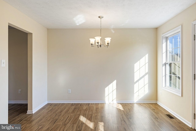 spare room featuring a chandelier, wood-type flooring, and a textured ceiling