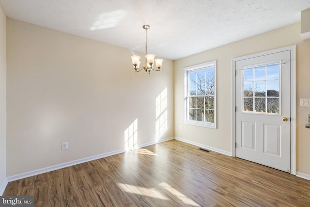 unfurnished dining area featuring an inviting chandelier, wood-type flooring, and a textured ceiling