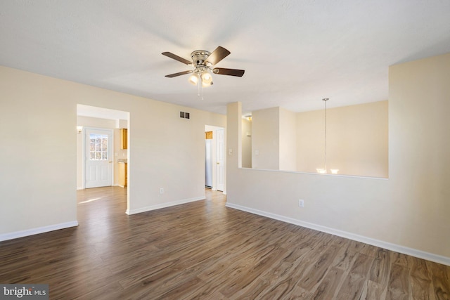 empty room featuring ceiling fan with notable chandelier and dark hardwood / wood-style flooring