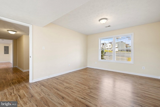 unfurnished room featuring hardwood / wood-style floors, electric panel, and a textured ceiling