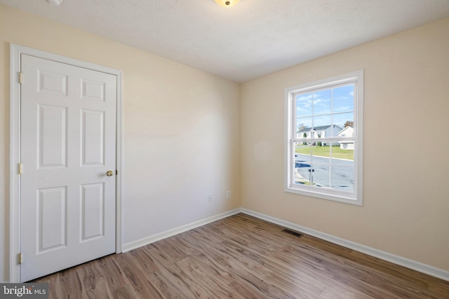 empty room with a textured ceiling and light hardwood / wood-style flooring