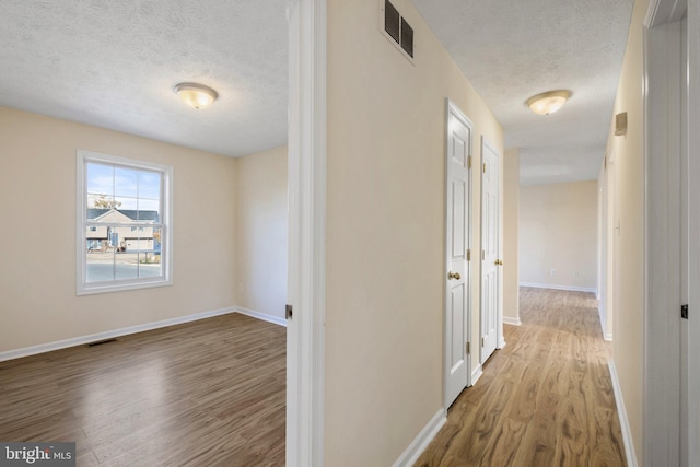 hall with light wood-type flooring and a textured ceiling