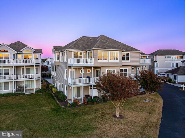 back house at dusk featuring a lawn and a balcony