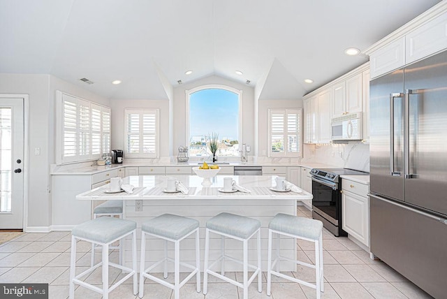 kitchen with a wealth of natural light, appliances with stainless steel finishes, vaulted ceiling, and a center island