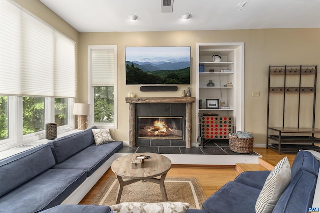 living room with built in shelves, a fireplace, and hardwood / wood-style floors