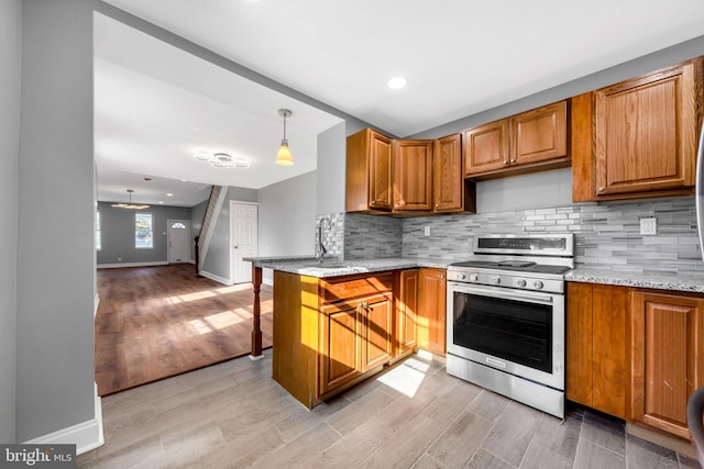 kitchen featuring light stone countertops, light wood-type flooring, kitchen peninsula, hanging light fixtures, and stainless steel stove