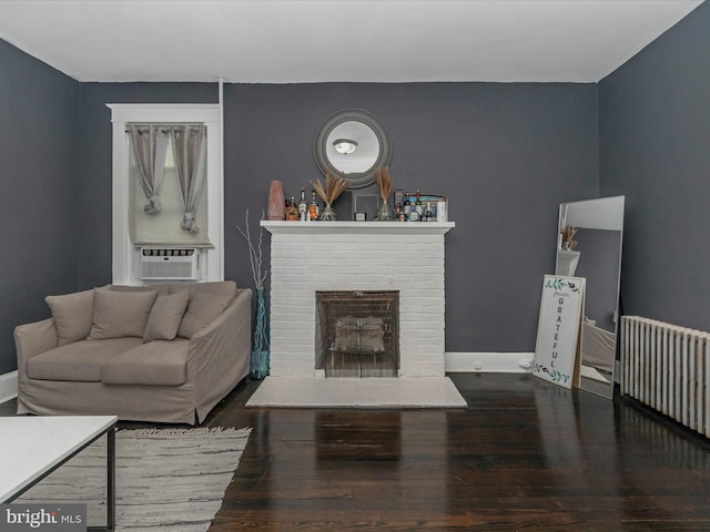 living room featuring radiator, hardwood / wood-style flooring, cooling unit, and a brick fireplace