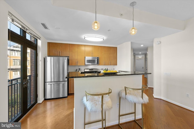 kitchen featuring appliances with stainless steel finishes, light wood-type flooring, decorative light fixtures, and a breakfast bar area