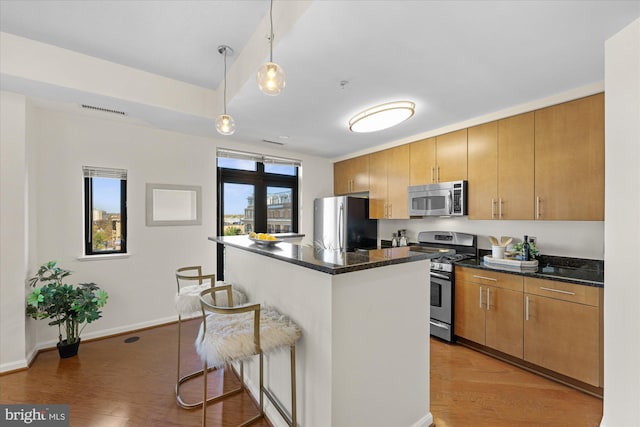 kitchen featuring stainless steel appliances, a kitchen breakfast bar, wood-type flooring, decorative light fixtures, and a kitchen island