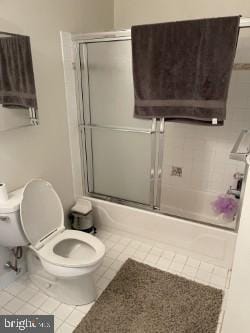 bathroom featuring tile patterned flooring, enclosed tub / shower combo, and toilet