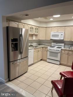 kitchen with light brown cabinetry, white appliances, sink, and light tile patterned floors