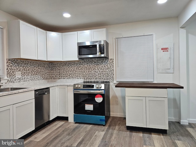 kitchen with tasteful backsplash, electric panel, appliances with stainless steel finishes, hardwood / wood-style floors, and white cabinets