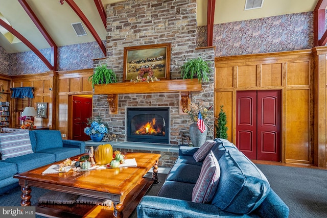 carpeted living room with beamed ceiling, wooden walls, a stone fireplace, and high vaulted ceiling