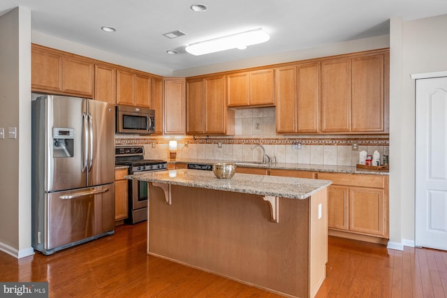 kitchen with stainless steel appliances, light stone countertops, backsplash, a center island, and dark hardwood / wood-style flooring