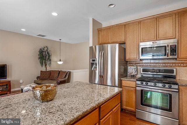 kitchen with appliances with stainless steel finishes, wood-type flooring, tasteful backsplash, and light stone countertops