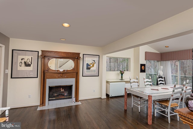 dining space with dark hardwood / wood-style flooring, vaulted ceiling, and a tiled fireplace