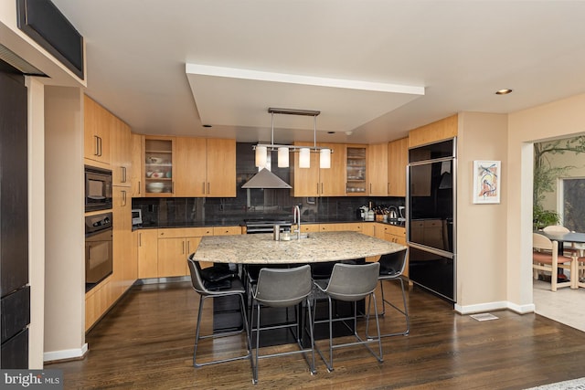 kitchen featuring black appliances, wall chimney exhaust hood, dark hardwood / wood-style flooring, and decorative backsplash