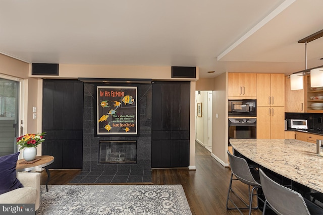 kitchen featuring light brown cabinets, black appliances, light stone countertops, decorative light fixtures, and dark hardwood / wood-style flooring