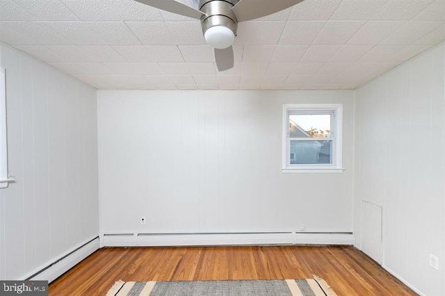 spare room featuring wood walls, baseboard heating, light wood-type flooring, and ceiling fan