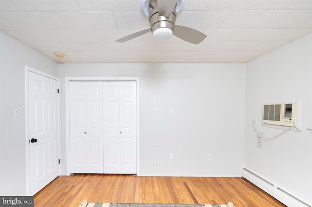 unfurnished bedroom with a baseboard heating unit, ceiling fan, wood-type flooring, a wall mounted air conditioner, and a closet