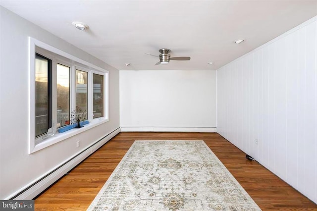 unfurnished room featuring a baseboard heating unit, wooden walls, wood-type flooring, and ceiling fan