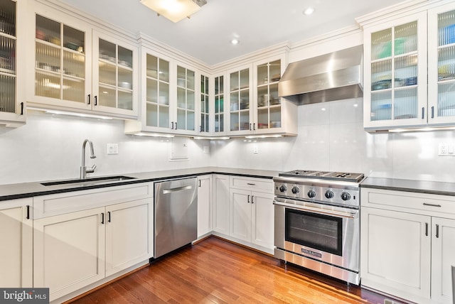 kitchen with sink, stainless steel appliances, wall chimney range hood, tasteful backsplash, and wood-type flooring