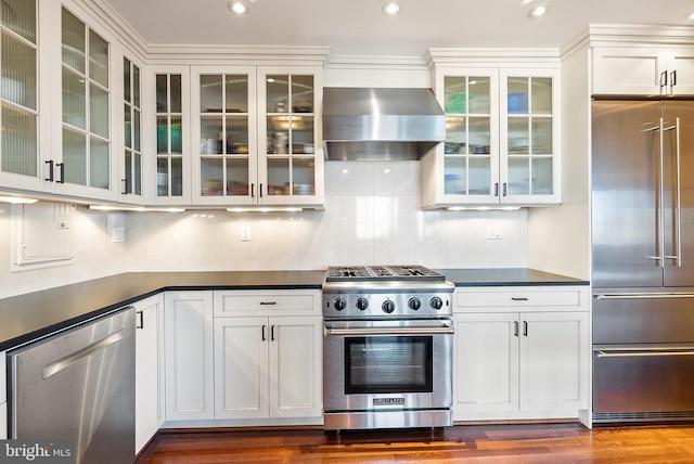 kitchen with white cabinets, dark hardwood / wood-style flooring, premium appliances, and wall chimney range hood