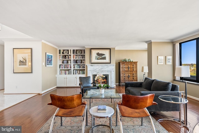 living room with hardwood / wood-style floors, built in shelves, ornamental molding, and a high end fireplace