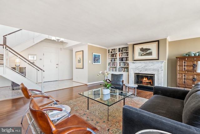 living room with built in features, light wood-type flooring, a fireplace, and ornamental molding