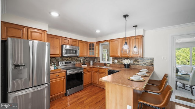 kitchen with appliances with stainless steel finishes, a peninsula, brown cabinets, glass insert cabinets, and light wood-style flooring