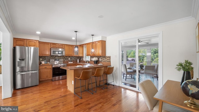 kitchen with appliances with stainless steel finishes, hardwood / wood-style flooring, a peninsula, decorative backsplash, and brown cabinetry