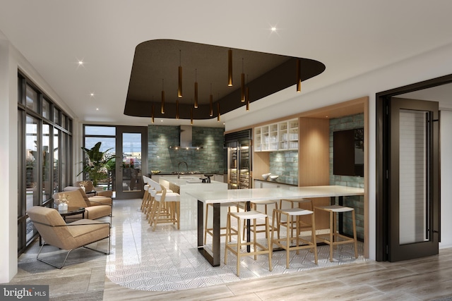 bar featuring wall chimney exhaust hood, built in fridge, a tray ceiling, sink, and tasteful backsplash