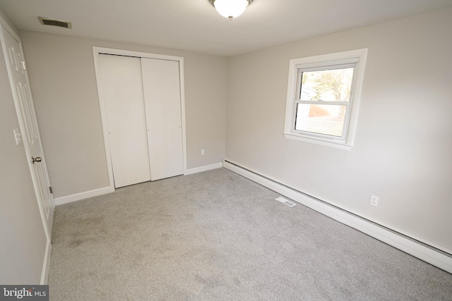 unfurnished bedroom with baseboard heating, light colored carpet, and a closet