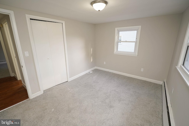 unfurnished bedroom with a baseboard heating unit, light carpet, and a closet