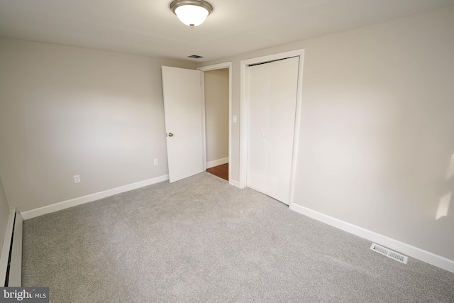 unfurnished bedroom with carpet, a baseboard heating unit, and a closet