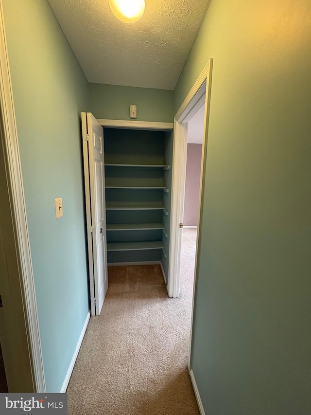 corridor with a textured ceiling and carpet flooring