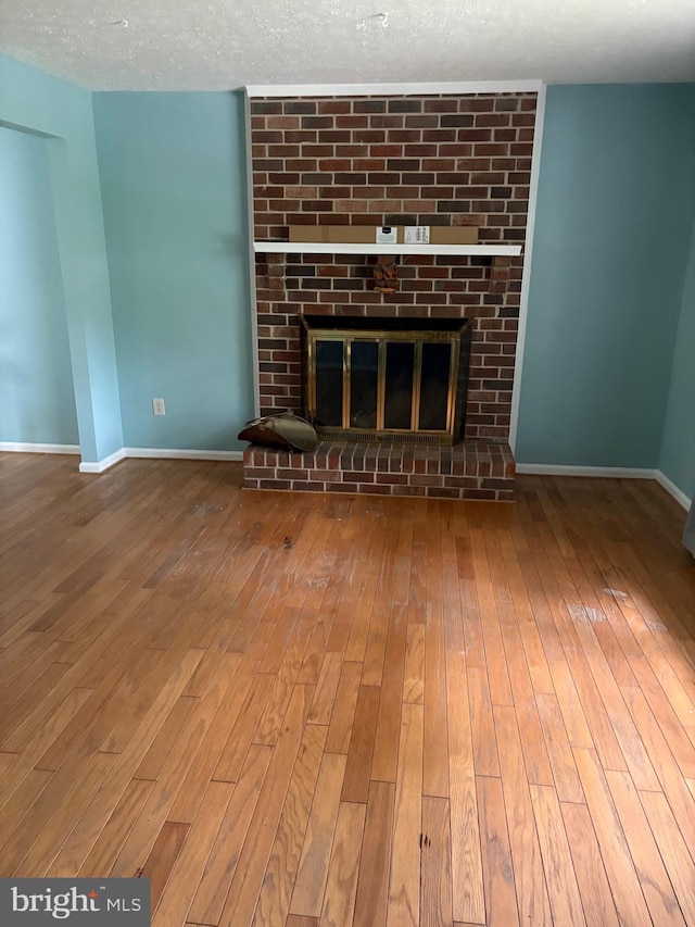 unfurnished living room featuring a textured ceiling, a brick fireplace, and wood-type flooring