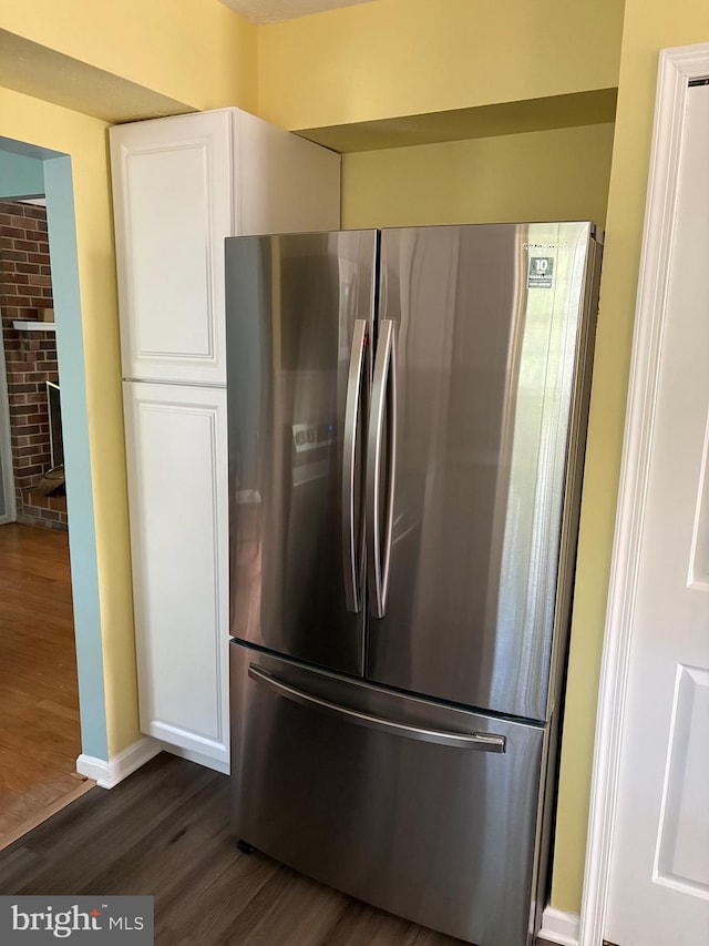 kitchen with stainless steel fridge, white cabinetry, a brick fireplace, and dark hardwood / wood-style floors