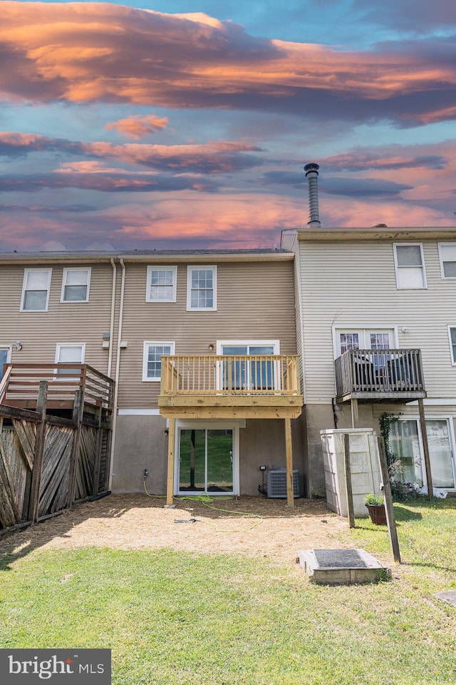 back house at dusk with a lawn, a balcony, and central AC unit