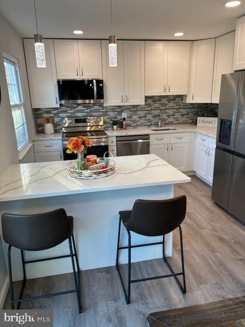 kitchen featuring appliances with stainless steel finishes, decorative light fixtures, light wood-type flooring, and white cabinets