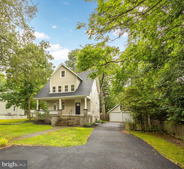 view of front of house featuring covered porch, a front yard, an outbuilding, and a garage