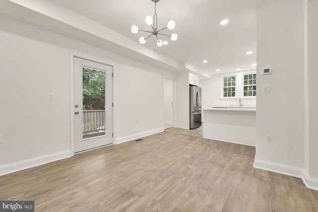 unfurnished living room featuring sink, a chandelier, and light hardwood / wood-style flooring