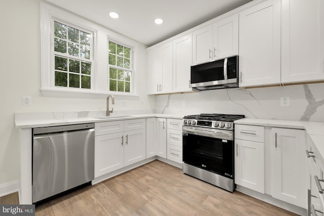 kitchen featuring decorative backsplash, stainless steel appliances, sink, white cabinetry, and light hardwood / wood-style floors