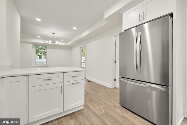 kitchen with stainless steel fridge, white cabinets, light stone counters, and light wood-type flooring