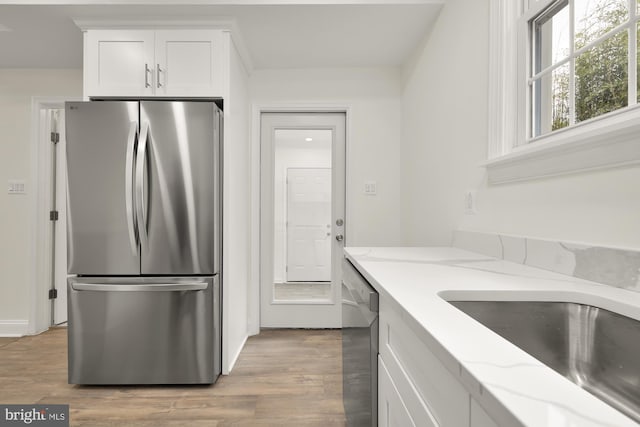 kitchen featuring light stone countertops, appliances with stainless steel finishes, sink, light hardwood / wood-style floors, and white cabinets