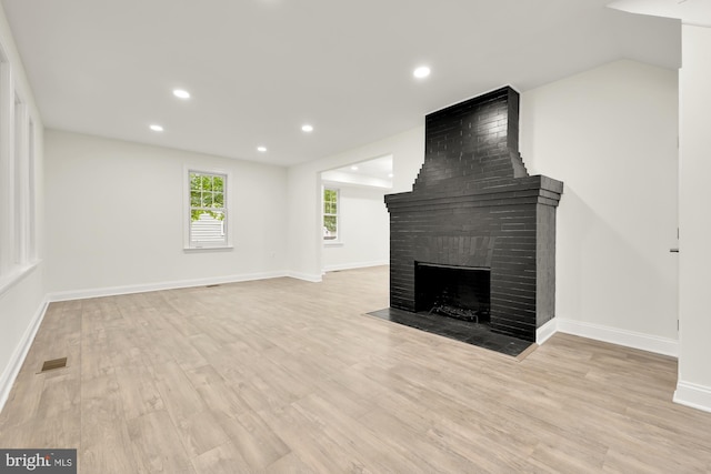 unfurnished living room with light hardwood / wood-style flooring and a brick fireplace