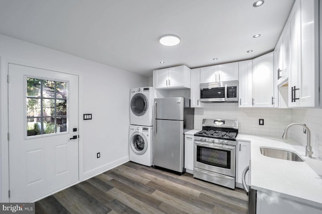 kitchen with stainless steel appliances, dark hardwood / wood-style flooring, stacked washing maching and dryer, sink, and white cabinetry