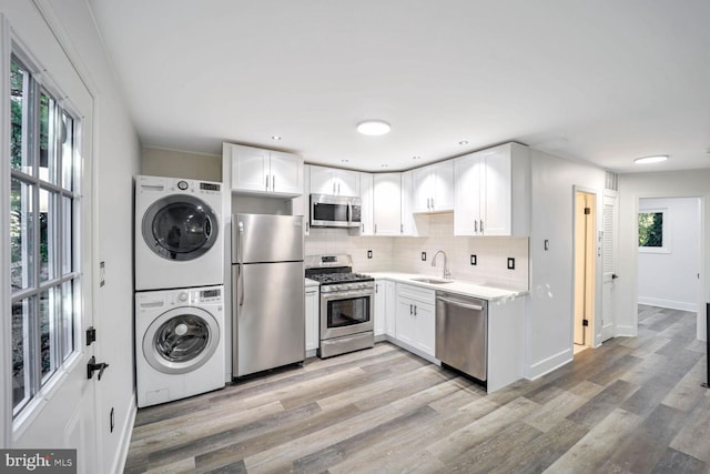 kitchen with white cabinets, a wealth of natural light, stacked washer / drying machine, and appliances with stainless steel finishes