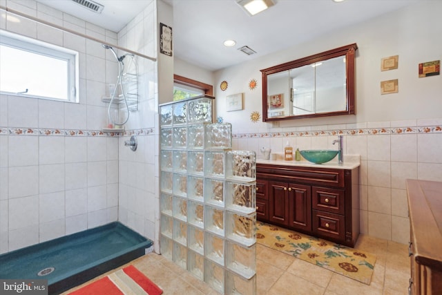 bathroom with a wealth of natural light, tiled shower, vanity, and tile walls