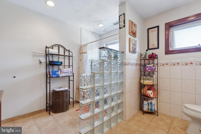 bathroom with toilet, a healthy amount of sunlight, walk in shower, and tile walls